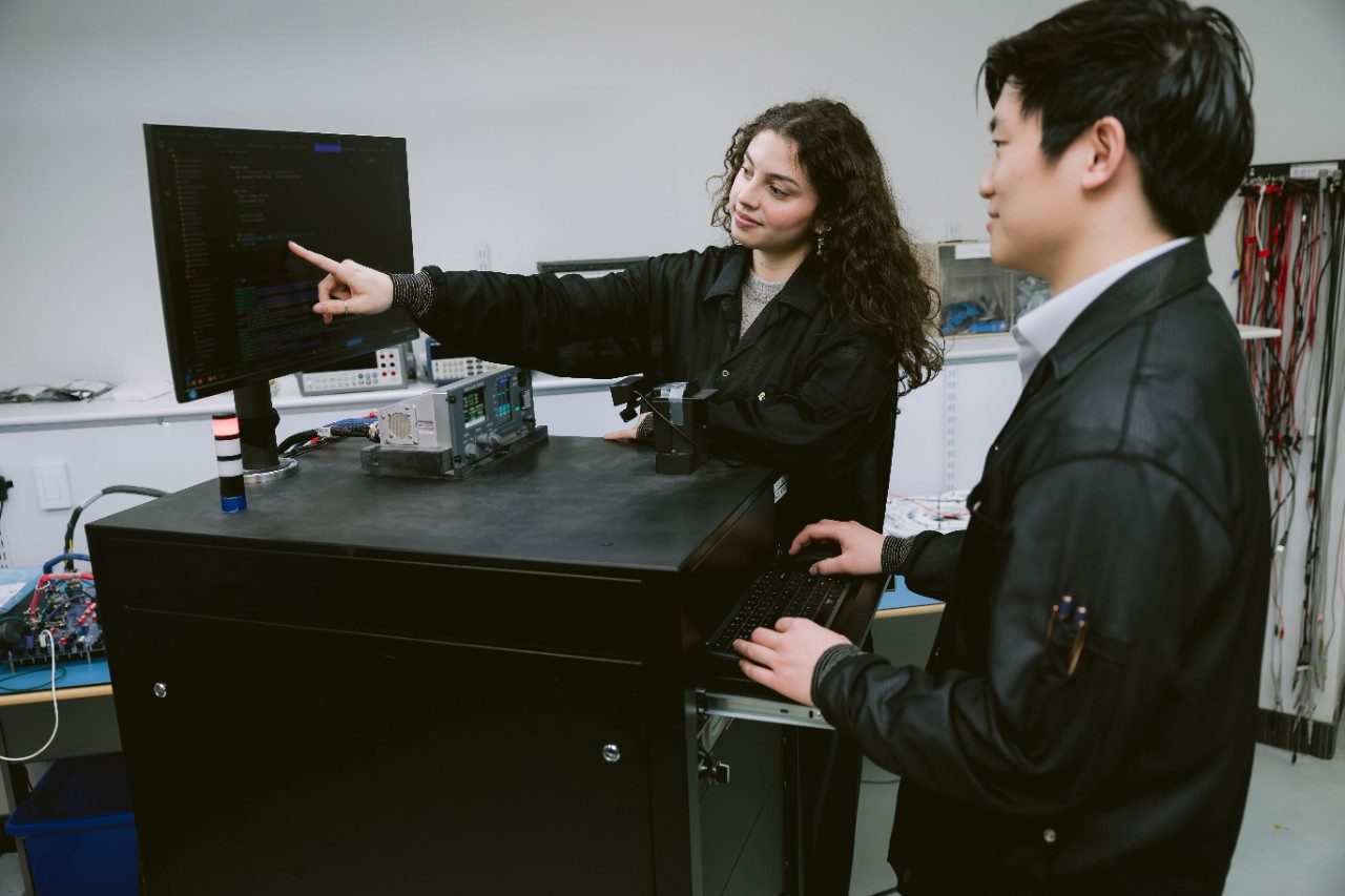Aversan employees, one pointing to a computer screen filled with lines of code as the other looks on